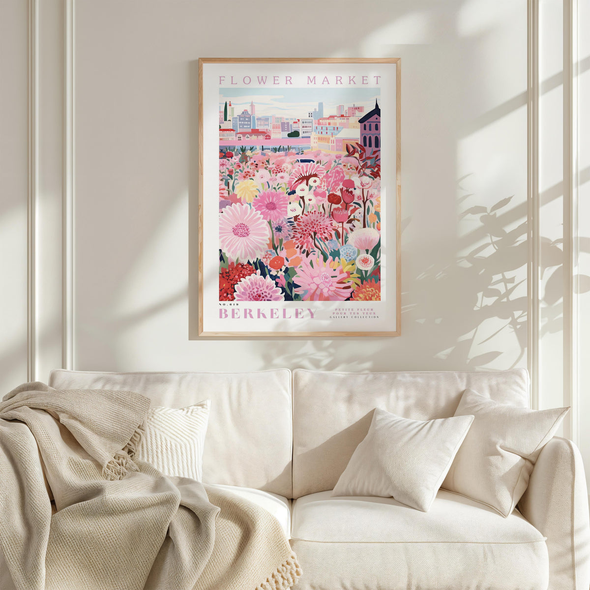 a framed poster of a colorful floral scene hanging on a wall above a white couch with a blanket draped over it.