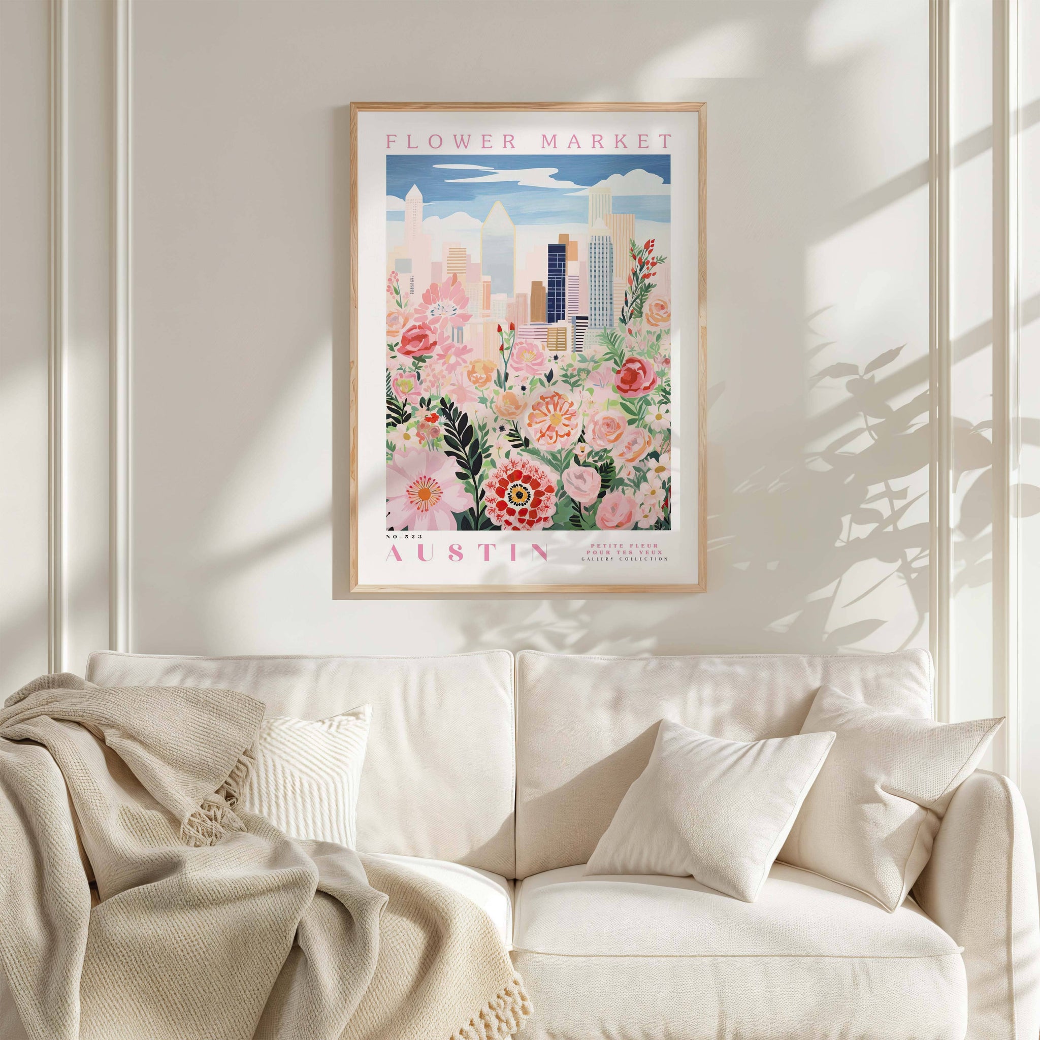 a framed poster of a cityscape with flowers hanging on a wall above a white couch with pillows.