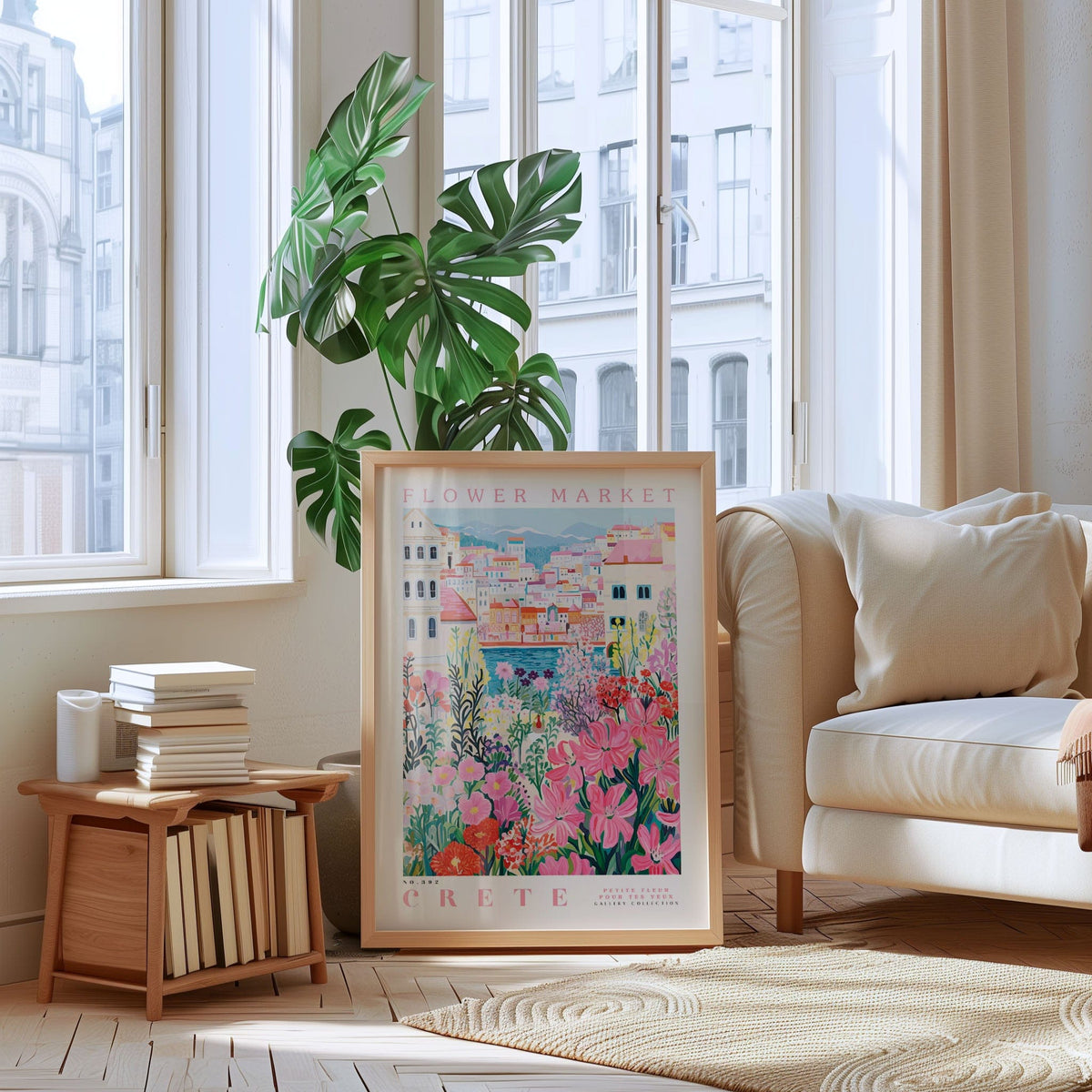 a living room with a large framed poster of a colorful floral scene hanging on the wall, a stack of books on a wooden table, a white sofa, and a large window overlooking a cityscape.