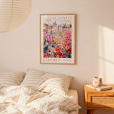 a bedroom scene with a framed poster of a colorful flower market hanging on the wall above a bed with striped pillows.