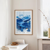 a framed poster of a mountainous landscape with a blue and white color scheme, hanging on a wall in a room with a white table and a window.