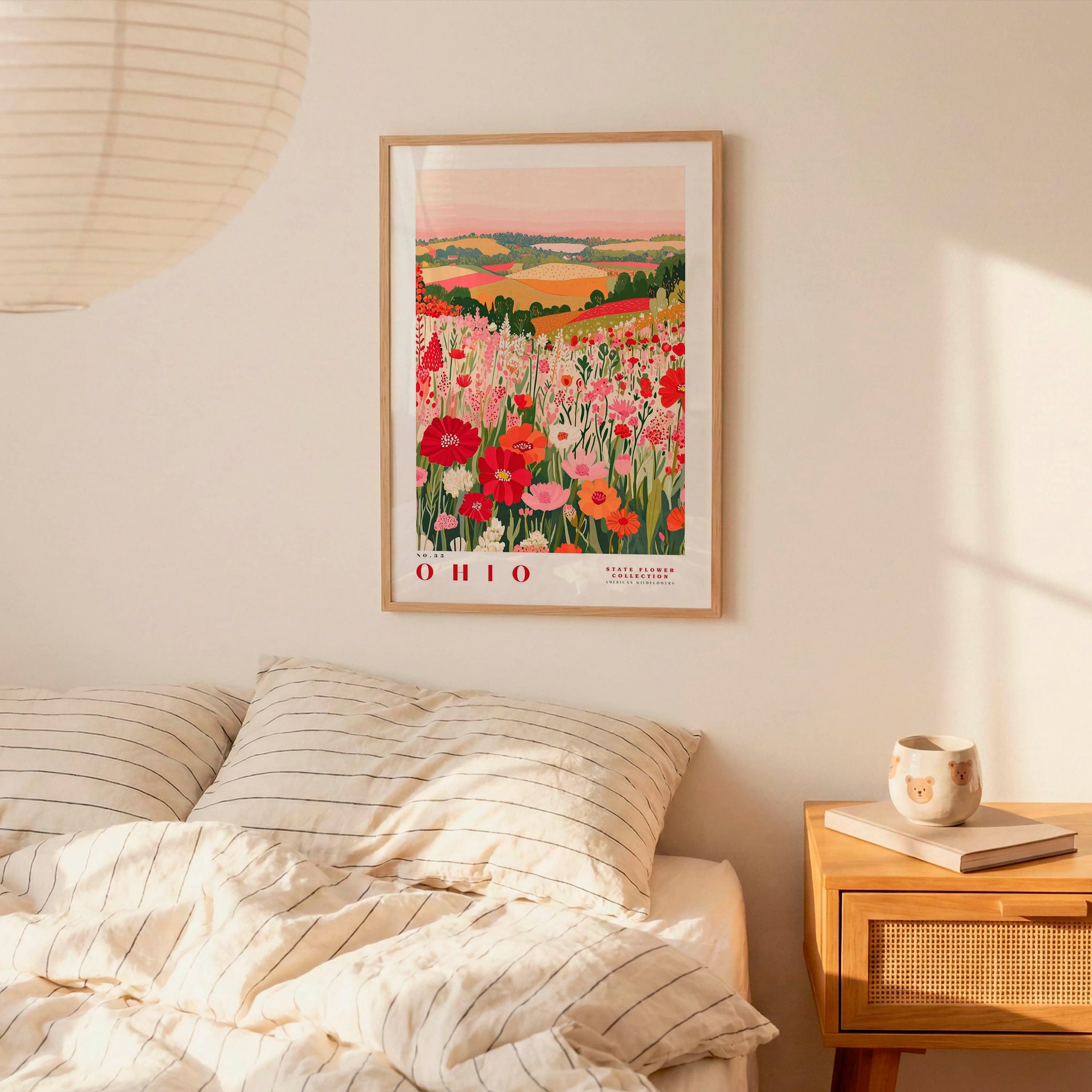 a bedroom scene with a framed poster of a field of flowers hanging on the wall above a bed with striped pillows.