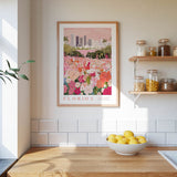 a framed poster of a colorful garden scene with flowers, hanging on a wall above a wooden countertop with a bowl of lemons.