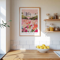 a framed poster of a colorful garden scene with flowers, hanging on a wall above a wooden countertop with a bowl of lemons.