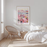 a bedroom with a bed, a woven chair, and a framed poster of a flower market on the wall.