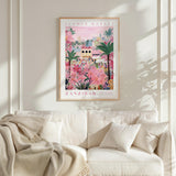 a poster of a flower market in Zanzibar hanging on a wall above a white couch with a blanket draped over it.
