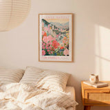 a framed poster of a cityscape with flowers hanging on a wall above a bed with striped pillows.
