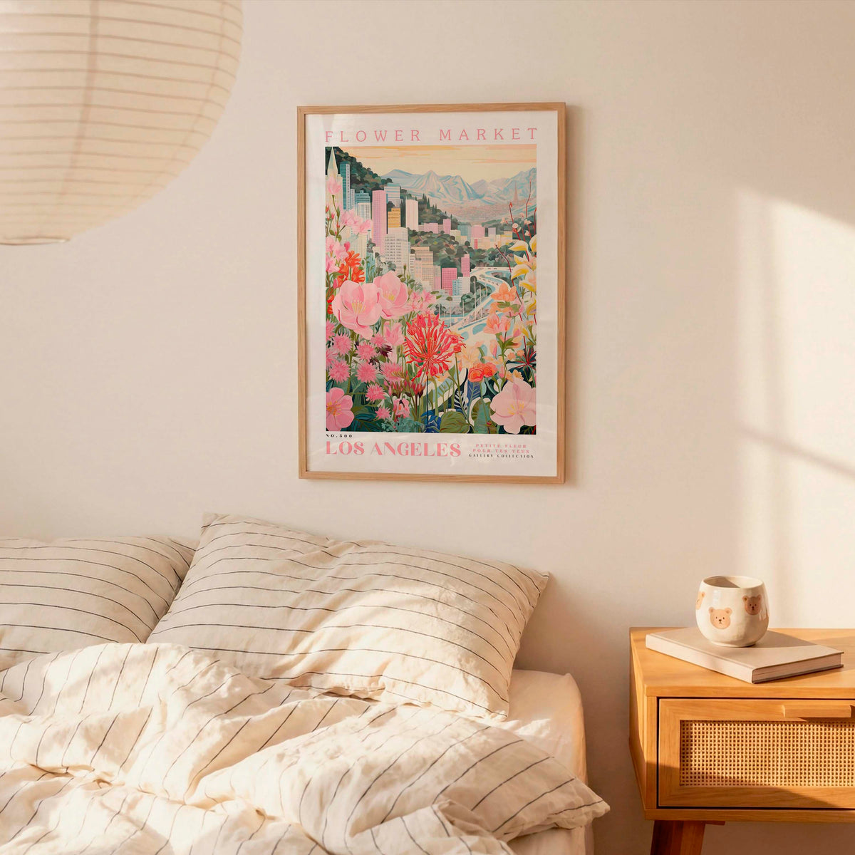 a framed poster of a cityscape with flowers hanging on a wall above a bed with striped pillows.