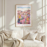 a framed poster of a colorful cityscape with flowers hanging on a wall above a white couch with pillows.