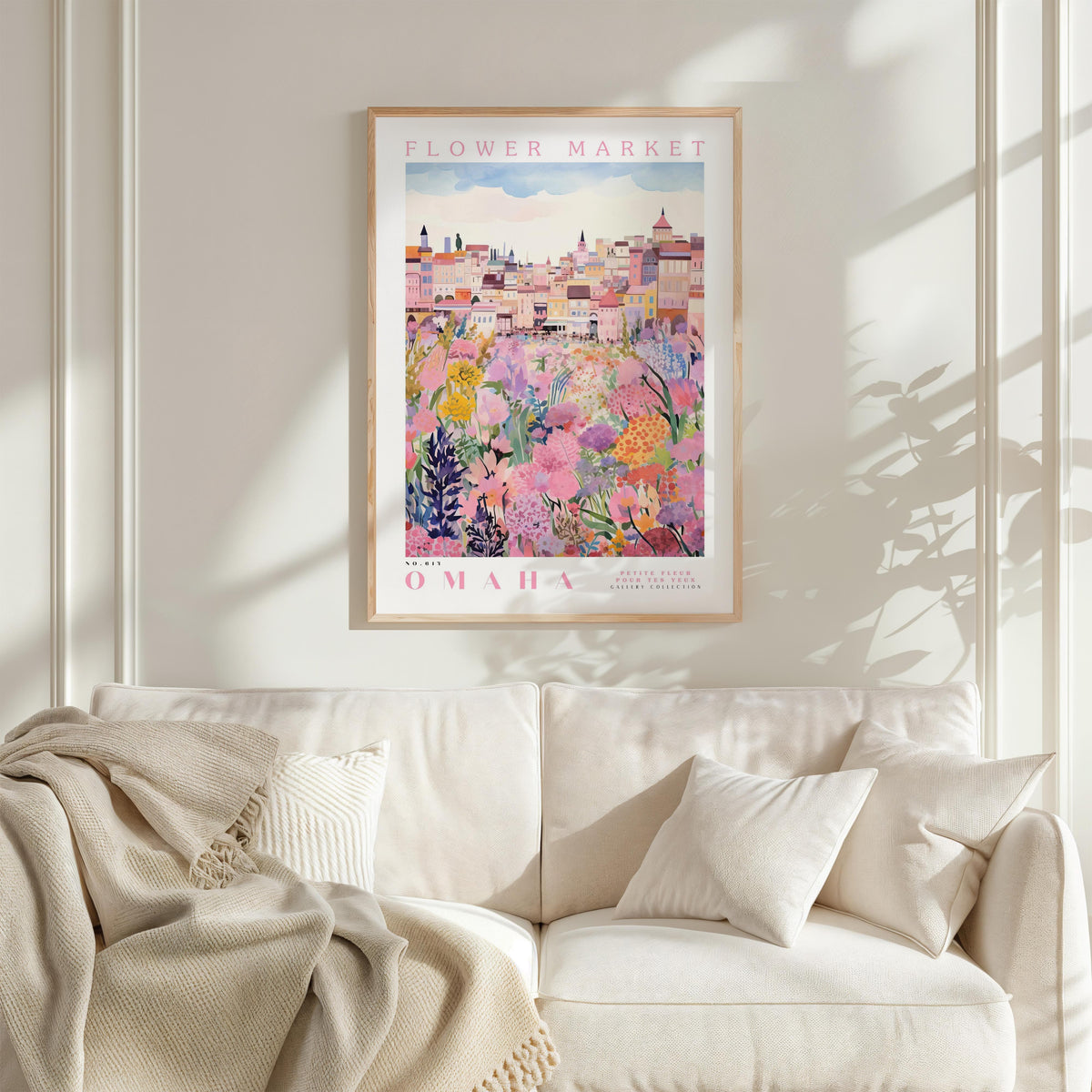 a framed poster of a colorful cityscape with flowers hanging on a wall above a white couch with pillows.
