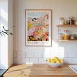 a framed poster of a colorful floral scene hanging on a wall above a wooden countertop with a bowl of lemons.