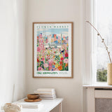 a framed poster of a colorful floral scene hanging on a wall, with a window and a small table with books and a vase in the foreground.