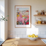 a kitchen scene with a framed poster of a colorful flower market in Nashville, Tennessee, hanging on the wall above a wooden counter. The poster displays a variety of flowers and plants, creating a vibrant and lively atmosphere. On the counter, there is a bowl of lemons, adding a touch of freshness to the scene. The kitchen also includes shelves with jars and bottles, suggesting a well-stocked and organized space.