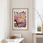a framed poster of a colorful floral scene hanging on a wall, with a window and a small table with books and a vase in the foreground.