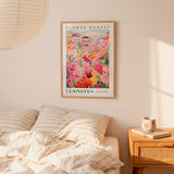 a framed poster of a flower market in Lexington, Kentucky, hanging on a wall above a bed with striped pillows.