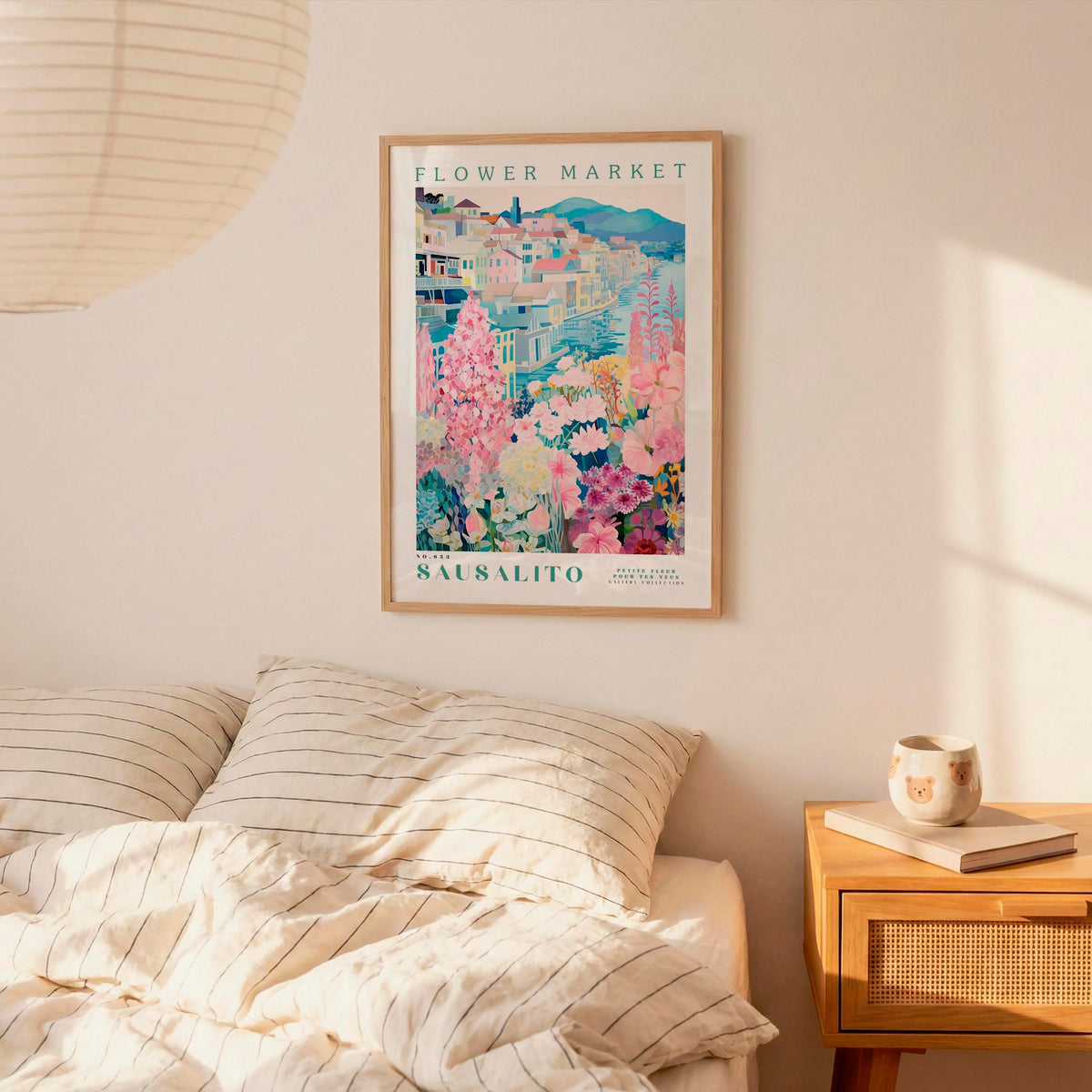 a bedroom setting with a framed poster of a colorful floral scene hanging on the wall above a bed with striped pillows.