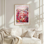 a framed poster of a vibrant floral scene hanging on a wall above a white couch with a blanket draped over it.