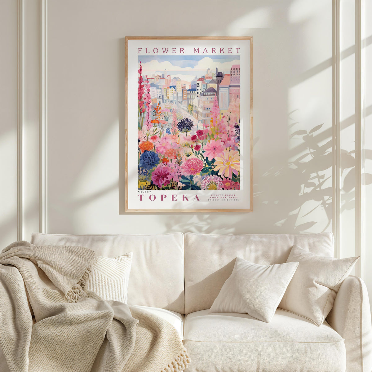 a framed poster of a colorful floral scene hanging on a wall above a white couch with a blanket draped over it.