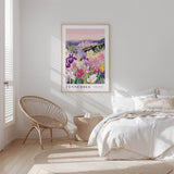 A bedroom with a large framed poster of a colorful floral scene hanging on the wall, a woven chair, and a bed with white bedding.