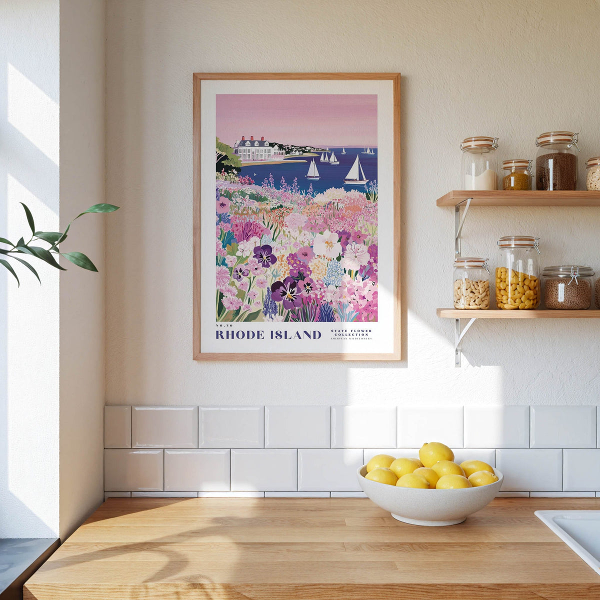 a kitchen scene with a framed poster of a colorful garden hanging on the wall above a wooden countertop. On the countertop, there is a bowl of lemons and a plant.