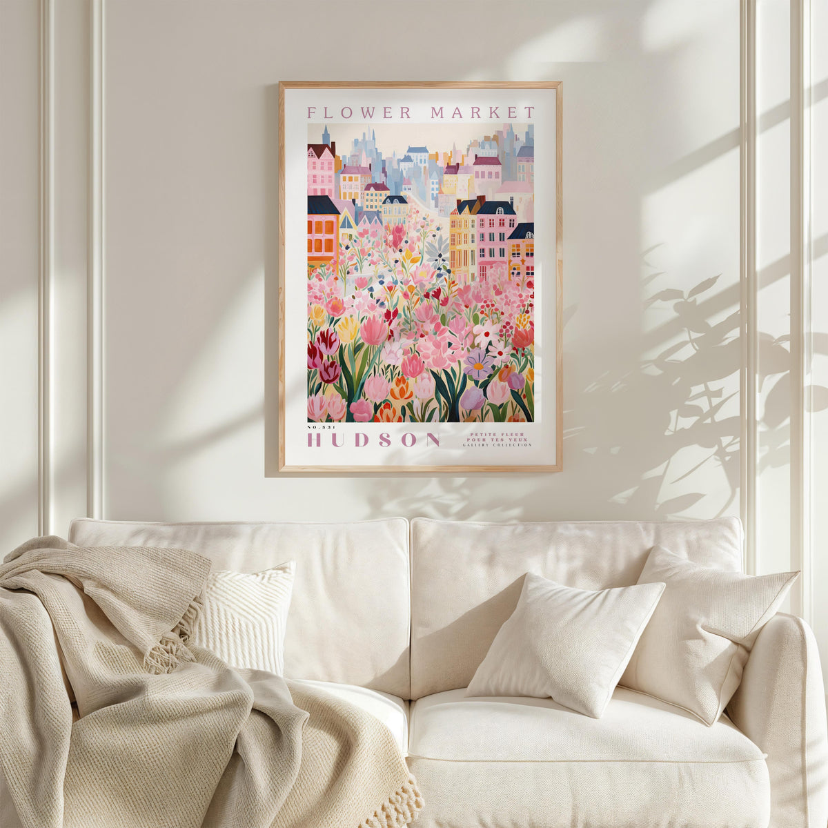 A framed poster of a colorful floral scene hangs on a wall above a white couch with a blanket draped over it.