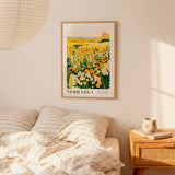 a bedroom scene with a framed poster of a field of flowers hanging on the wall above a bed with striped pillows.