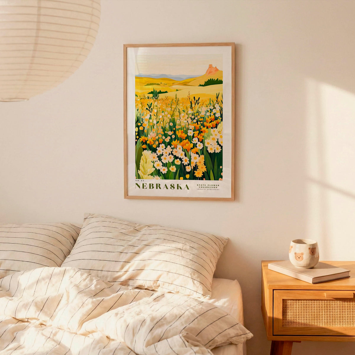 a bedroom scene with a framed poster of a field of flowers hanging on the wall above a bed with striped pillows.