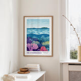 a framed poster of a vibrant underwater scene, depicting a coral reef with various marine life, hanging on a wall in a room with a white table and a window.
