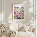 a framed poster of a colorful garden scene hanging on a wall above a white couch.