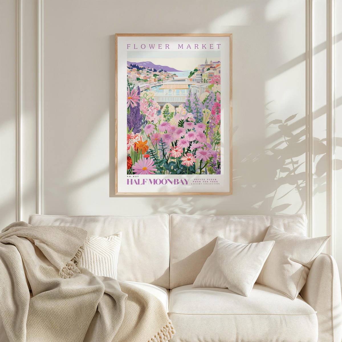 a framed poster of a colorful garden scene hanging on a wall above a white couch.