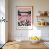 a framed poster of a scenic landscape with a lake and mountains, hanging on a wall above a wooden counter with a bowl of lemons.