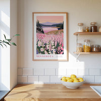 a framed poster of a scenic landscape with a lake and mountains, hanging on a wall above a wooden counter with a bowl of lemons.