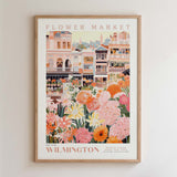 The image is a framed poster depicting a vibrant and colorful flower market in Wilmington, with buildings, flowers, and greenery surrounding the scene.