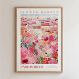 The image is a framed poster depicting a vibrant and colorful scene of a flower market in a city, with buildings and flowers in shades of pink, red, and yellow.