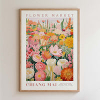The image is a framed poster of a vibrant and colorful flower market, featuring a variety of flowers and plants in different shades of pink, orange, yellow, and white.
