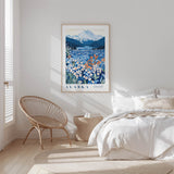 A bedroom with a large framed poster of a mountain landscape with flowers hanging on the wall, a woven chair, and a bed with white bedding.
