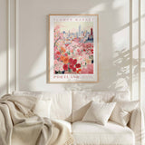 a framed poster of a cityscape with a flower market in Portland, Oregon, hanging on a wall above a white couch with a blanket draped over it.