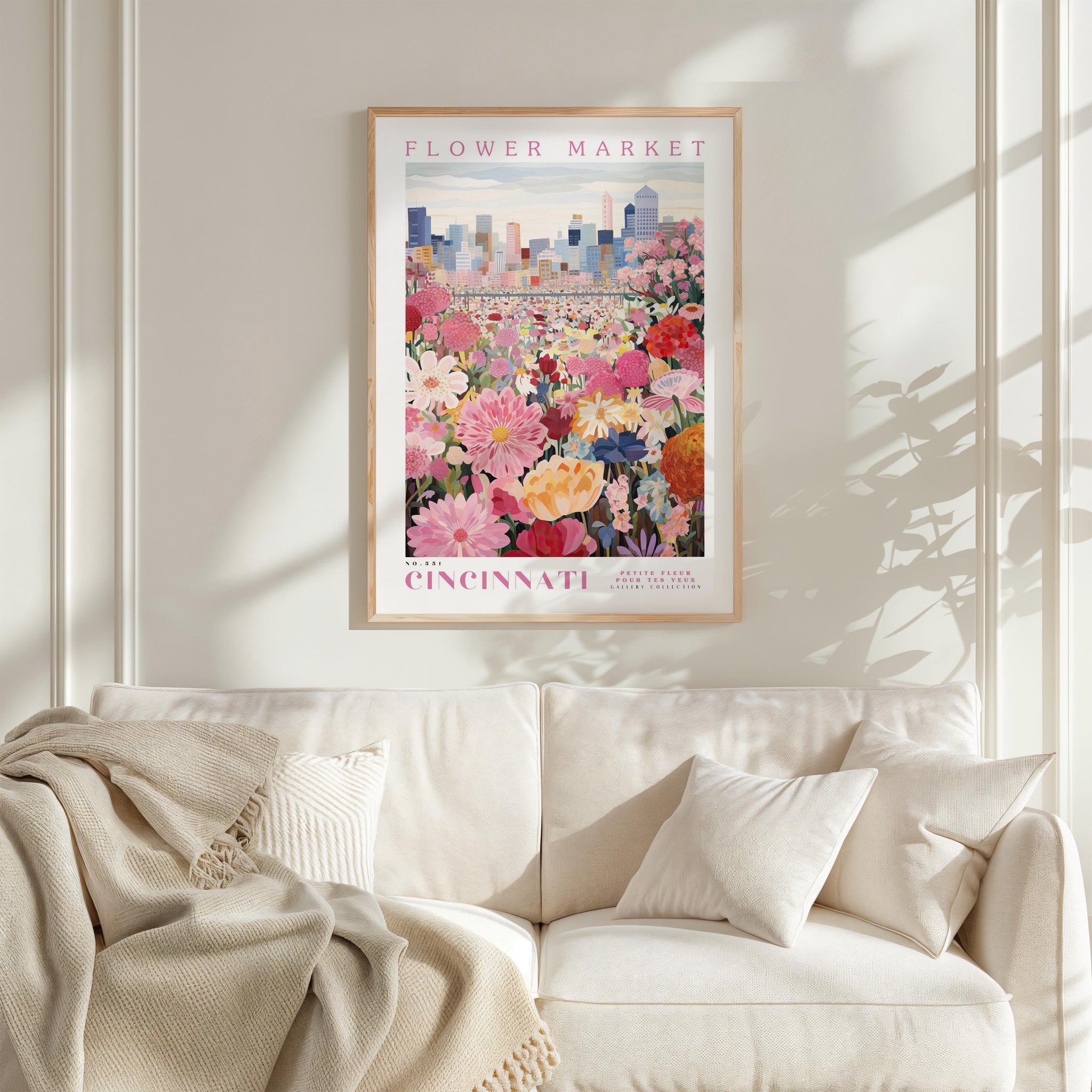 a poster of a flower market in Cincinnati hanging on a wall above a white couch with a blanket draped over it.