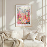 a framed poster of a colorful garden scene hanging on a wall above a white couch.