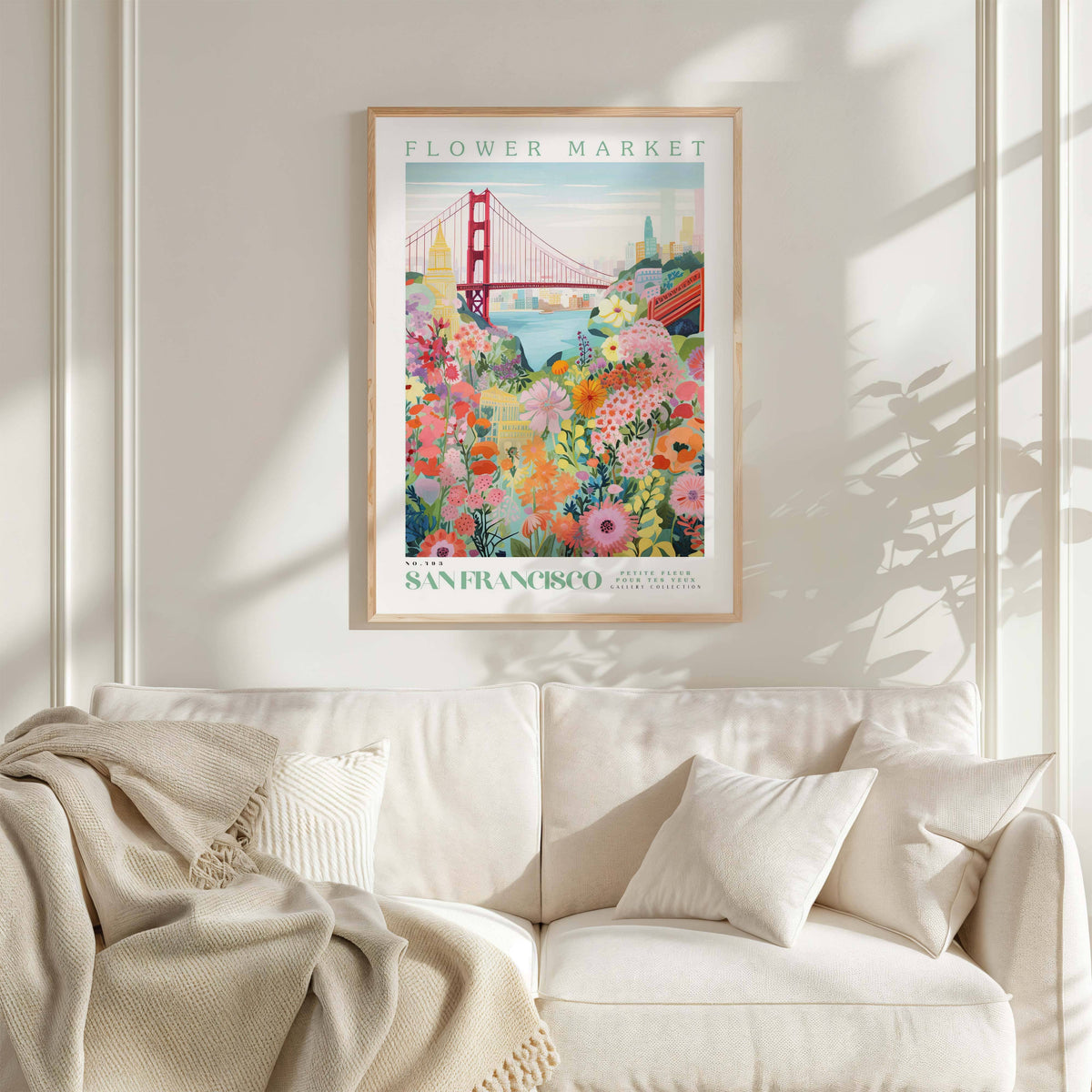 a framed poster of the Golden Gate Bridge and a colorful floral scene, hanging on a wall above a white couch with a blanket draped over it.
