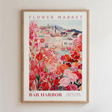 The image is a framed poster depicting a vibrant and colorful scene of a flower market in a town, with buildings, flowers, and a river in the background.