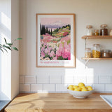 a framed poster of a mountain landscape with pink flowers hanging on a wall above a wooden countertop with a bowl of lemons.