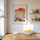 a framed poster of a desert landscape with cacti and flowers, hanging on a wall above a wooden countertop with a bowl of lemons.