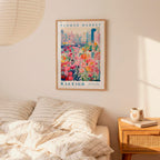 a framed poster of a colorful floral scene hanging on a wall above a bed with striped pillows.