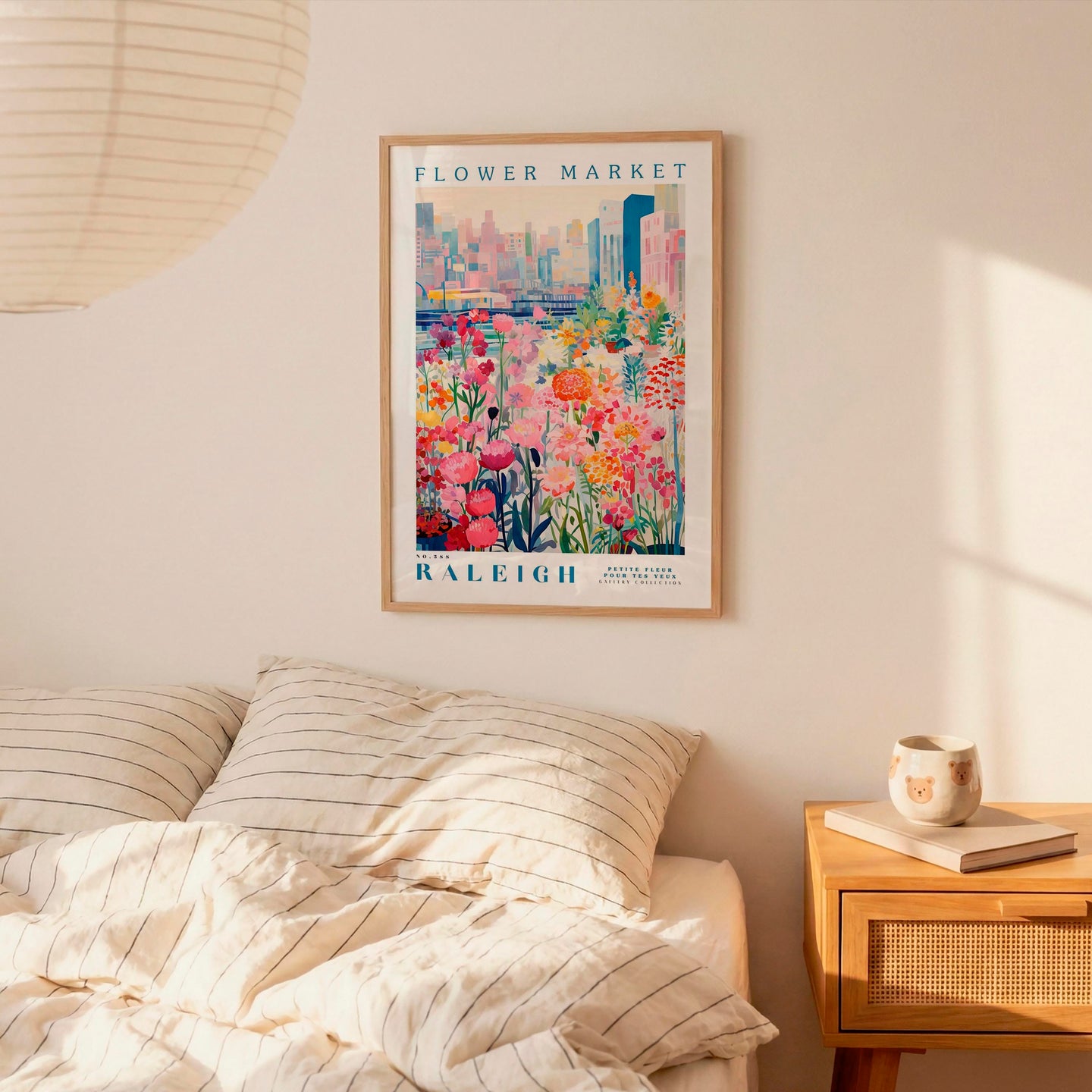 a framed poster of a colorful floral scene hanging on a wall above a bed with striped pillows.