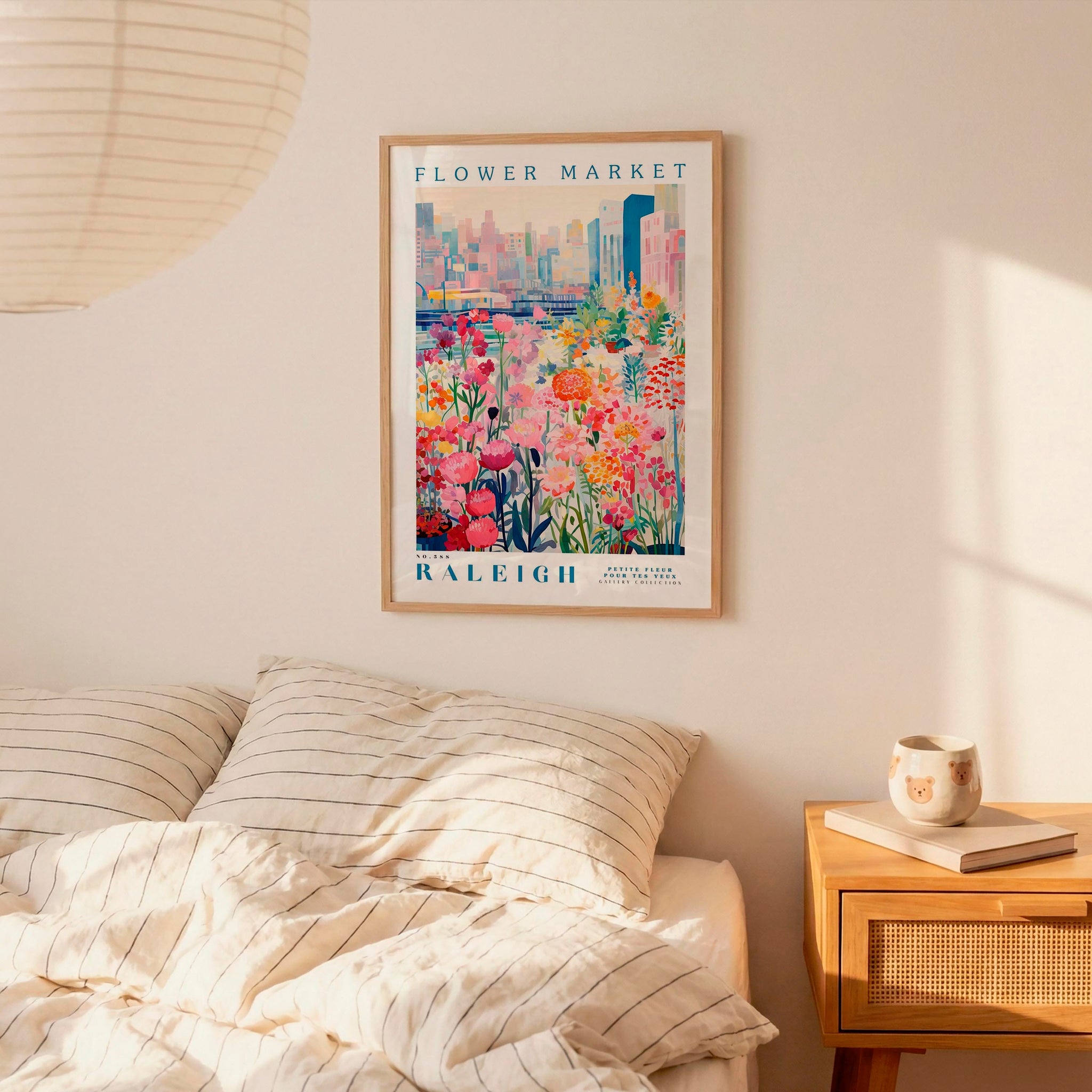 a framed poster of a colorful floral scene hanging on a wall above a bed with striped pillows.