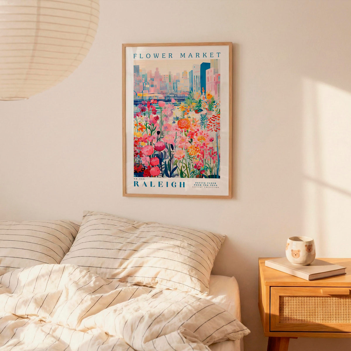 a framed poster of a colorful floral scene hanging on a wall above a bed with striped pillows.
