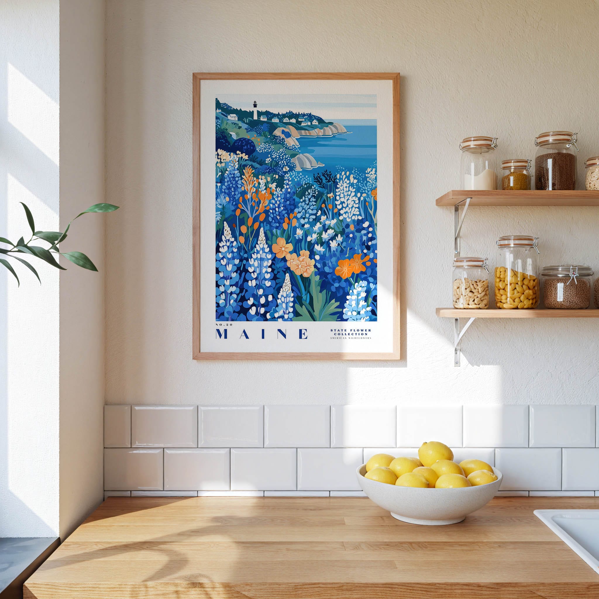 a framed poster of a coastal landscape with a lighthouse, hanging on a wall above a wooden countertop with a bowl of lemons.