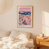 a bedroom setting with a framed poster of a colorful coastal scene hanging on the wall above a bed with striped pillows.