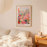 a bedroom scene with a framed poster of a flower market hanging on the wall above a bed with striped pillows.